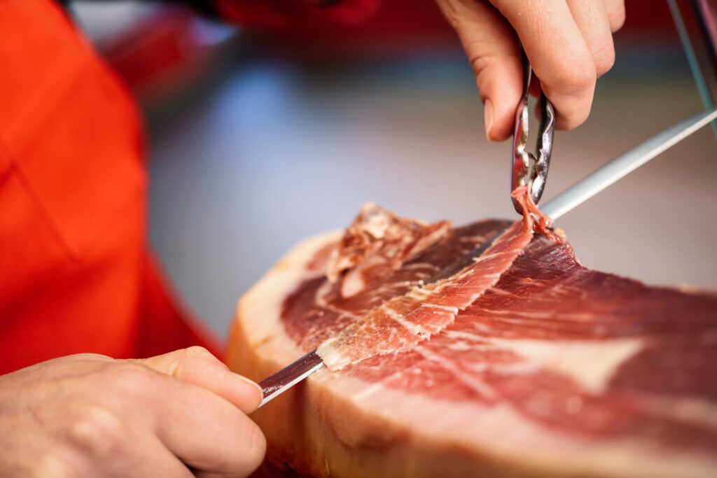 https://images.enriquetomas.com/blog/wp-content/uploads/2022/06/professional-cutter-carving-slices-from-whole-bone-serrano-ham-1024x683.jpg